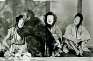 Three figures sit wearing white masks, while a man embraces the figure on the left