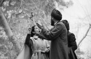 A woman in a trench coat in animated conversation with a man in a head wrap