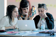 Three women look over a laptop together