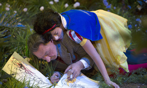 A figure dressed as Snow White lies on top of a man drawing in the grass