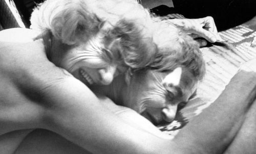 Still from the film "Nitrate Kisses" (1992), showing two naked women lying face down, one on top of the other, both smiling.