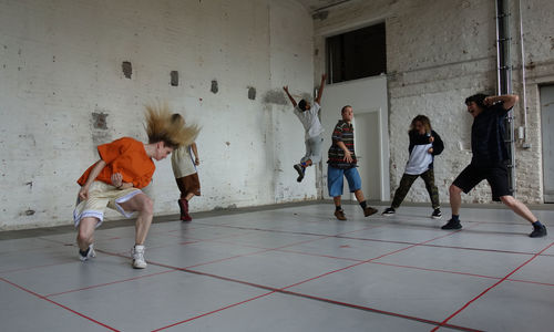 Six people dancing expressively in a studio with white brick walls and floor with a grid