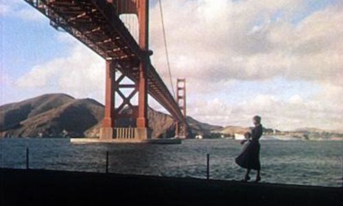 A woman stands at the waterfront in front of the Golden Gate Bridge