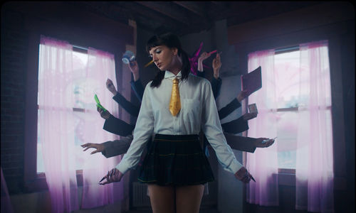Film still of a video showing a White woman in a schoolgirl uniform with multiple arms haloing her