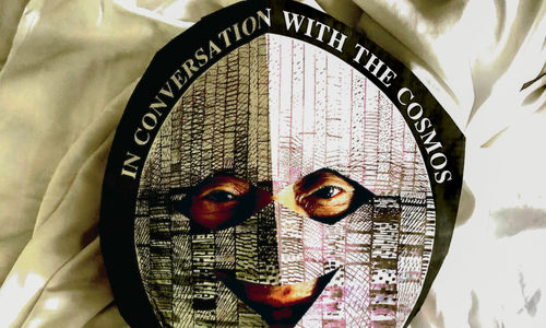 Photo of David Medalla wearing a mask that reads "in conversation with the cosmos"