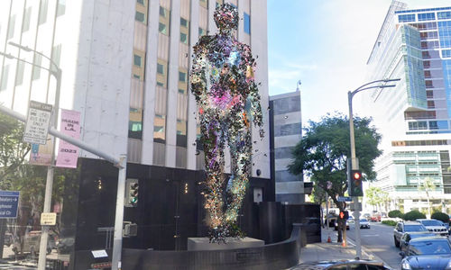 Rendering of a towering digital sculpture of a figure standing on an outdoor plinth