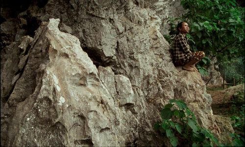 A man perches on a large, craggy rock