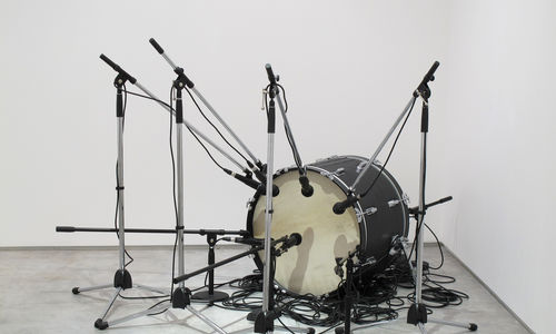 A bass drum sits on the floor surrounded by an array of microphones