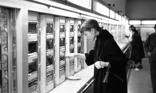 Black and white photo of Audrey Hepburn inspecting items in an automat