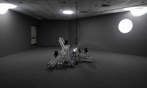 A metal installation at the center, with light and shadow in the background.