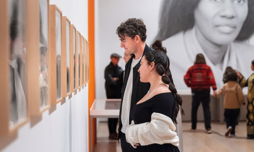 Visitors viewing a row of framed works installed on a gallery wall