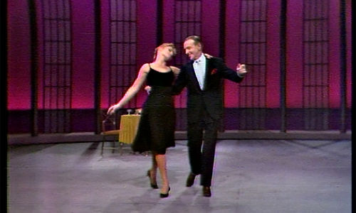 Fred Astaire dances arm-in-arm with a woman in a black dress