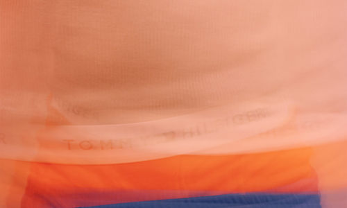 Blurred image of a torso wearing blue shorts with orange boxers peaking above the waistband, the white band of the underwear reading "TOMMY HILFIGER" in black letters