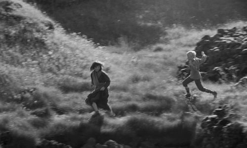 girl and boy running through field, b&w