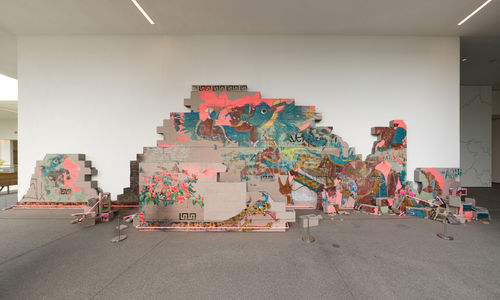 Installation featuring a crumbling wall of cinderblocks with handpainted images and pink neon lights