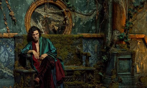 Oscar Isaac as Dr. Frankenstein, dressed in lush robes, sits pensively on a bench overgrown with weeds