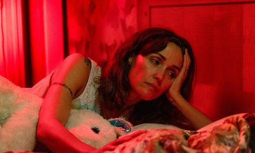 Rose Byrne lays in a bed holding a stuffed animal
