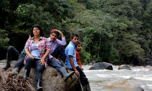 Berta Cáceres and four young men sit on a boulder in a river