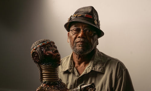 The artists Akinsanya Kambon sits next to his sculpture of a long-necked figure