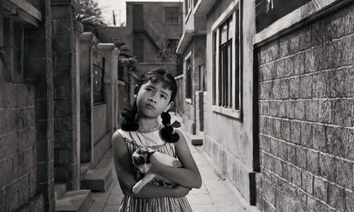 A girl standing in an alley, holding a cat in her arms