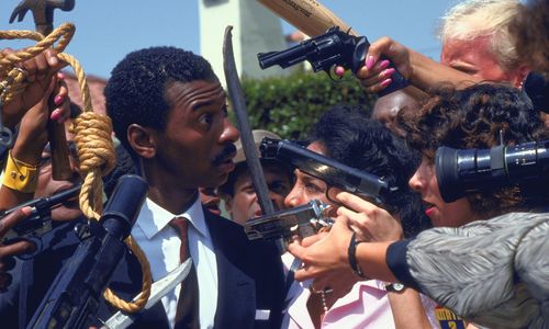 A Black man in a suit is surrounded by press