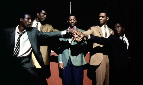 Five Black men stand in a semi-circle, their hands joined in the center