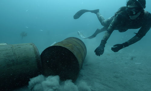 A diver encounters large metal barrels on the sea floor