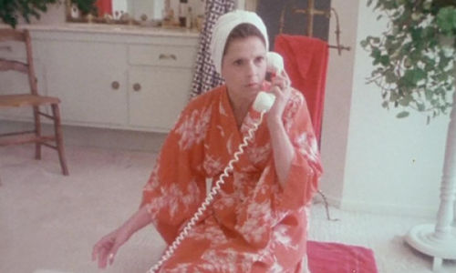 A woman in a pink robe kneels on the phone as she talks into a telephone