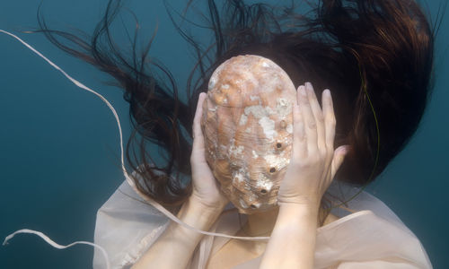 A woman, underwater, holds a large shell in front of her face