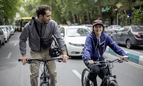 A young man and woman bike down a city street