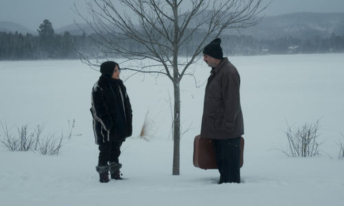 A woman and a man holding a suitcase, standing in a snowy landscape