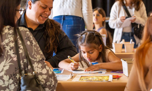 Child draws at a table while adults look on