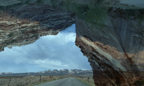 A onpen road on a barren landscape framed by canyons.