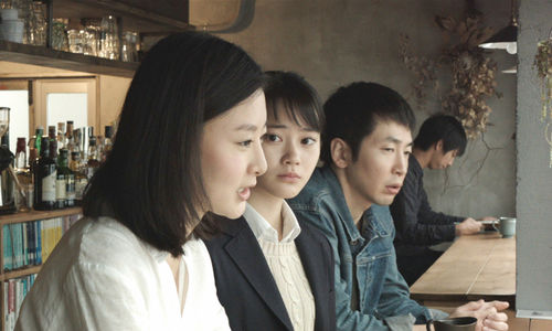 Two women and a man, viewed in profile, sit at a bar counter