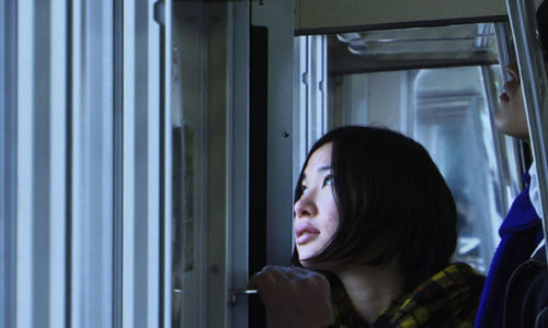 A woman with a short, dark bob haircut looks out of a window