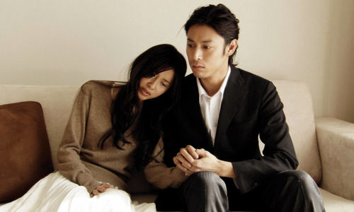 A mand and woman sit on a couch holding hands