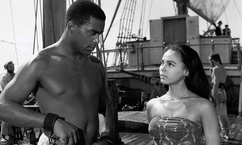 A man and woman looking at each other on a ship. The man is enslaved in shackles.