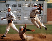 Still from the film Eight Men Out (1988) showing a baseball player slide into a base while another player, on the White Sox team, jumps and throws a ball to complete a double-play while a third player looks on