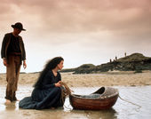 Still from the film The Secret of Roan Inish (1994) showing a woman crouching in the water, over a floating bassinet , with a man standing nearby