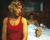 Still from the film Sunshine State (2002) showing a woman sitting in the foreground at the edge of a bed, and a man half-covered by a sheet sitting up against the headboard