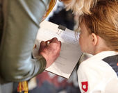 A young girl looks at a piece of paper while someone writes on it