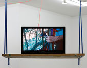 An open laptop computer sits on a wooden shelf that hangs from the ceiling. The walls in the background are white, and the edge of an open skylight are visible at the top right of the image.  