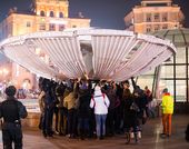 Several people attempt to touch a tall trumpeting structure in the center of a fountain.