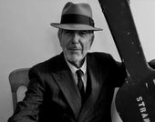 Black and white photo of musician Leonard Cohen seated with his arm around a guitar case