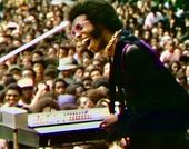 Still from the documentary film "Summer of Soul" (2021) showing Sly Stone performing in front of a large crowd