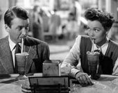 A man and woman make eye contact while sipping on milk shakes. 