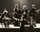 Black and white still from the film "The Last Waltz" (1978) showing a band performing with a conductor