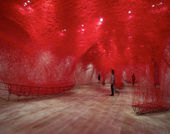 A huge intricate net of red thread creates a mesh over the gallery. Only coming down to connect with these iron wireframes of boats.