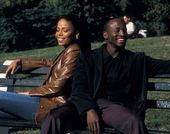 Man and woman sit back to back laughing on park bench