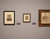 A gallery wall with three Van Gogh works on paper hung on it, and didactic labels. The wall is painted a neutral brown grey and the prints are all dark brown lines on parchment colored paper.